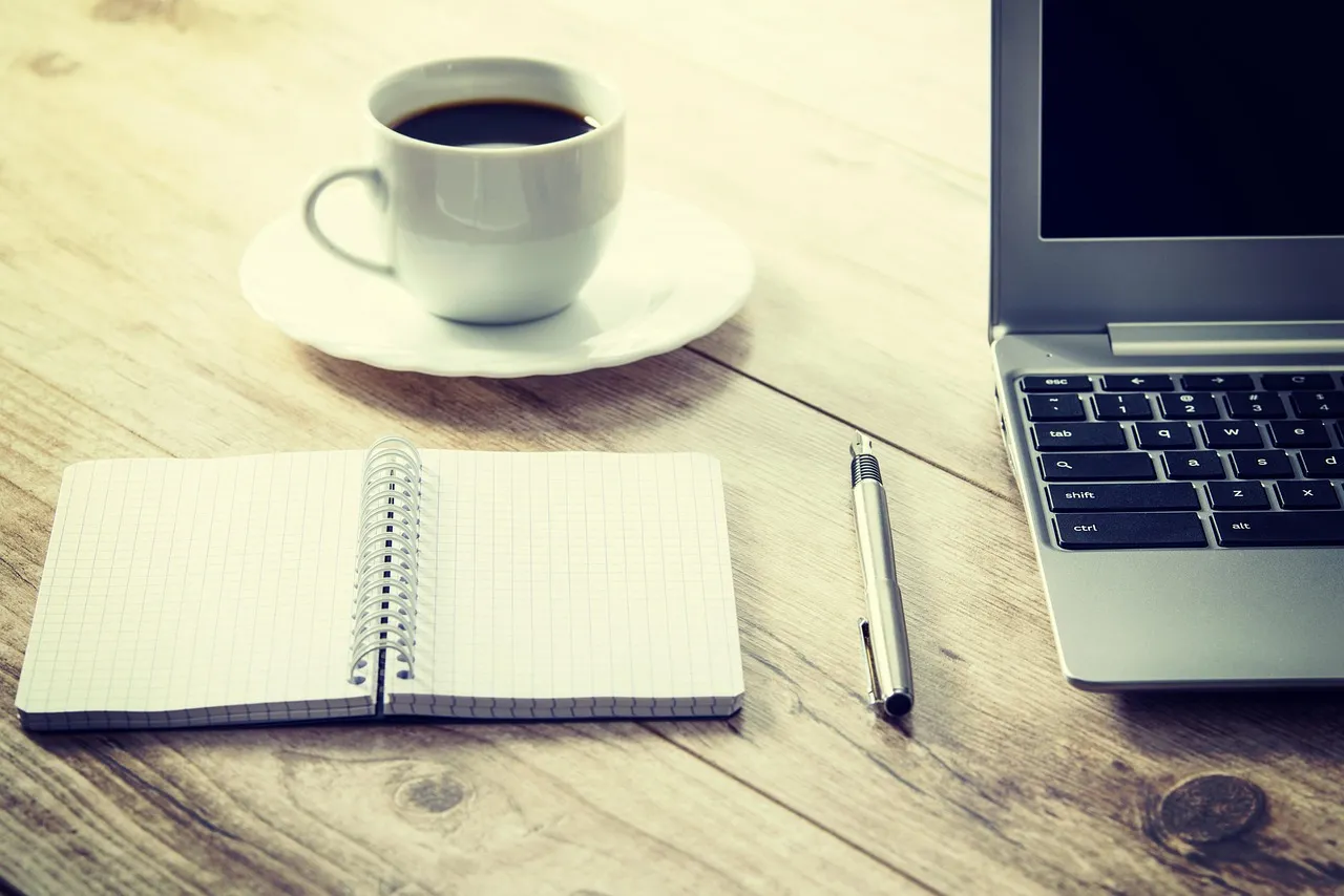 Arbeitsplatz mit Laptop, Notizbuch und Kaffeetasse auf Holztisch