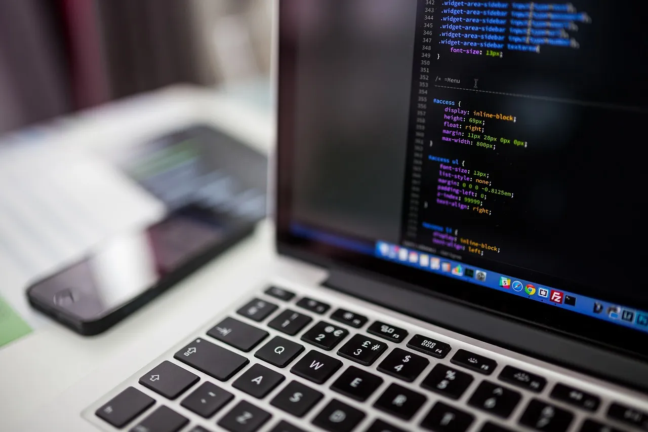 Laptop mit Programmcode, daneben ein Smartphone