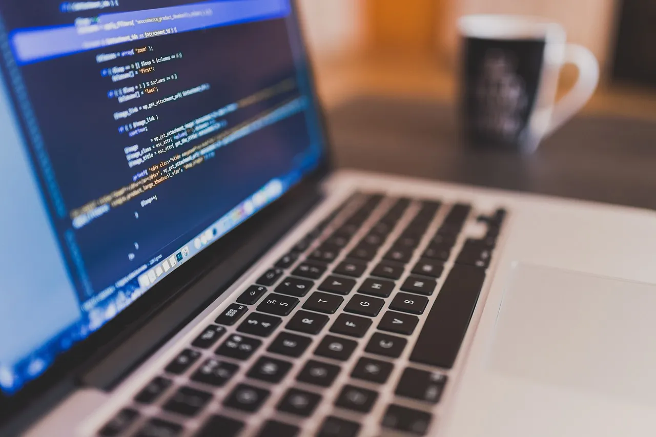 Laptop mit Programmcode auf einem Holztisch, daneben eine Kaffeetasse
