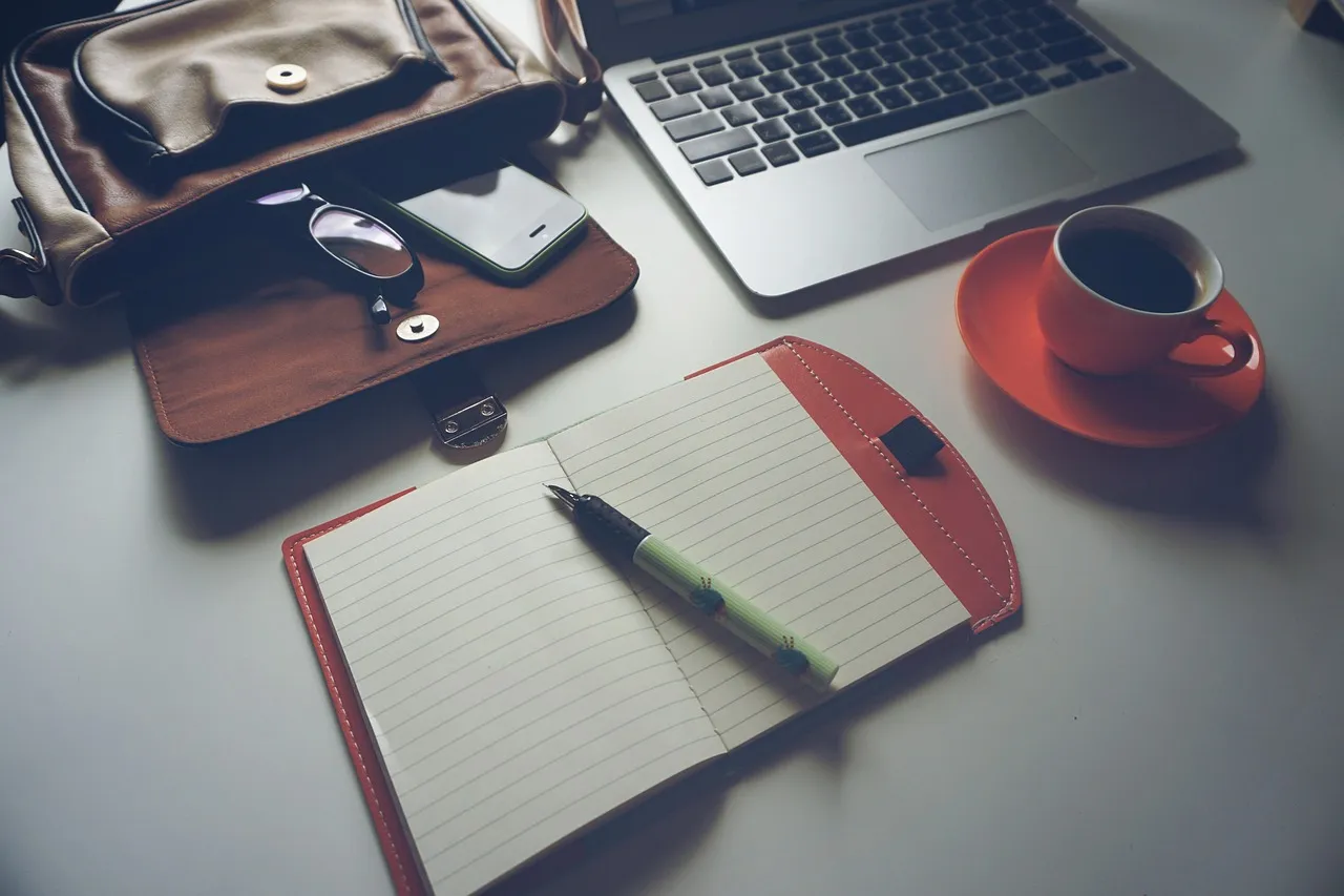 Notizbuch, Laptop und Kaffee auf dem Schreibtisch